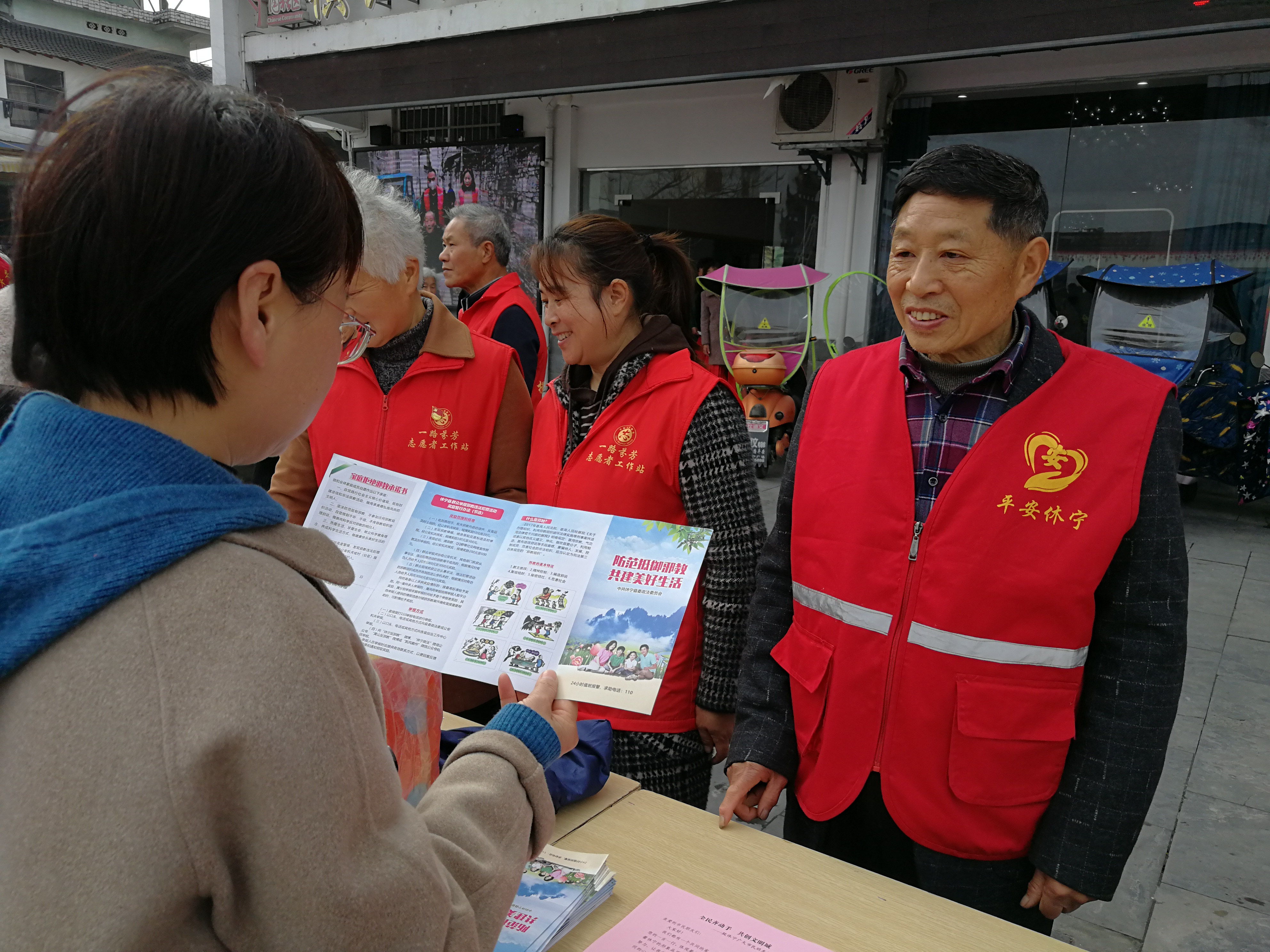 平安休宁志愿者向群众发放反邪教宣传册，现场群众在认真学习和咨询了解反邪教常识，表示今后积极参与反邪教斗争